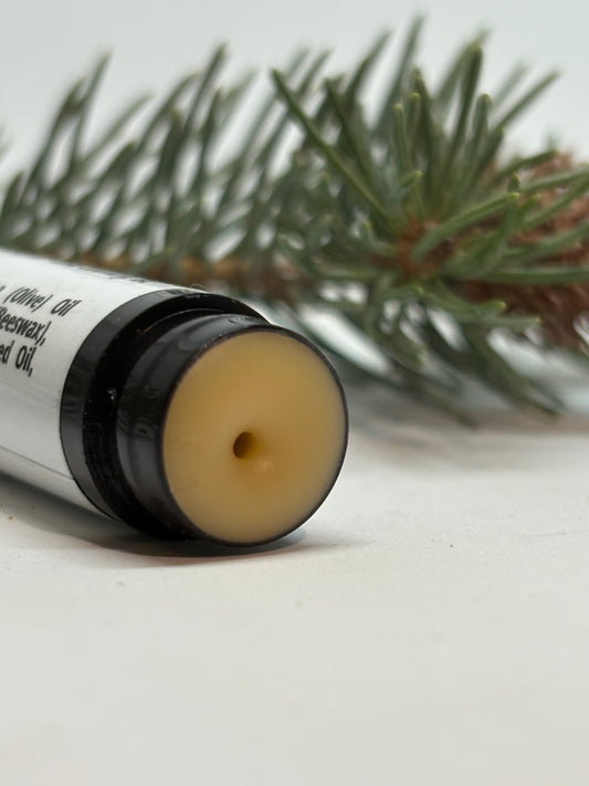 Close-up of Pine Pitch Lip Balm tip showing texture, with pine sprig in background
