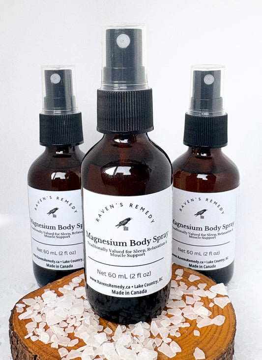 Raven’s Remedy magnesium body spray bottles on a wooden surface with magnesium flakes